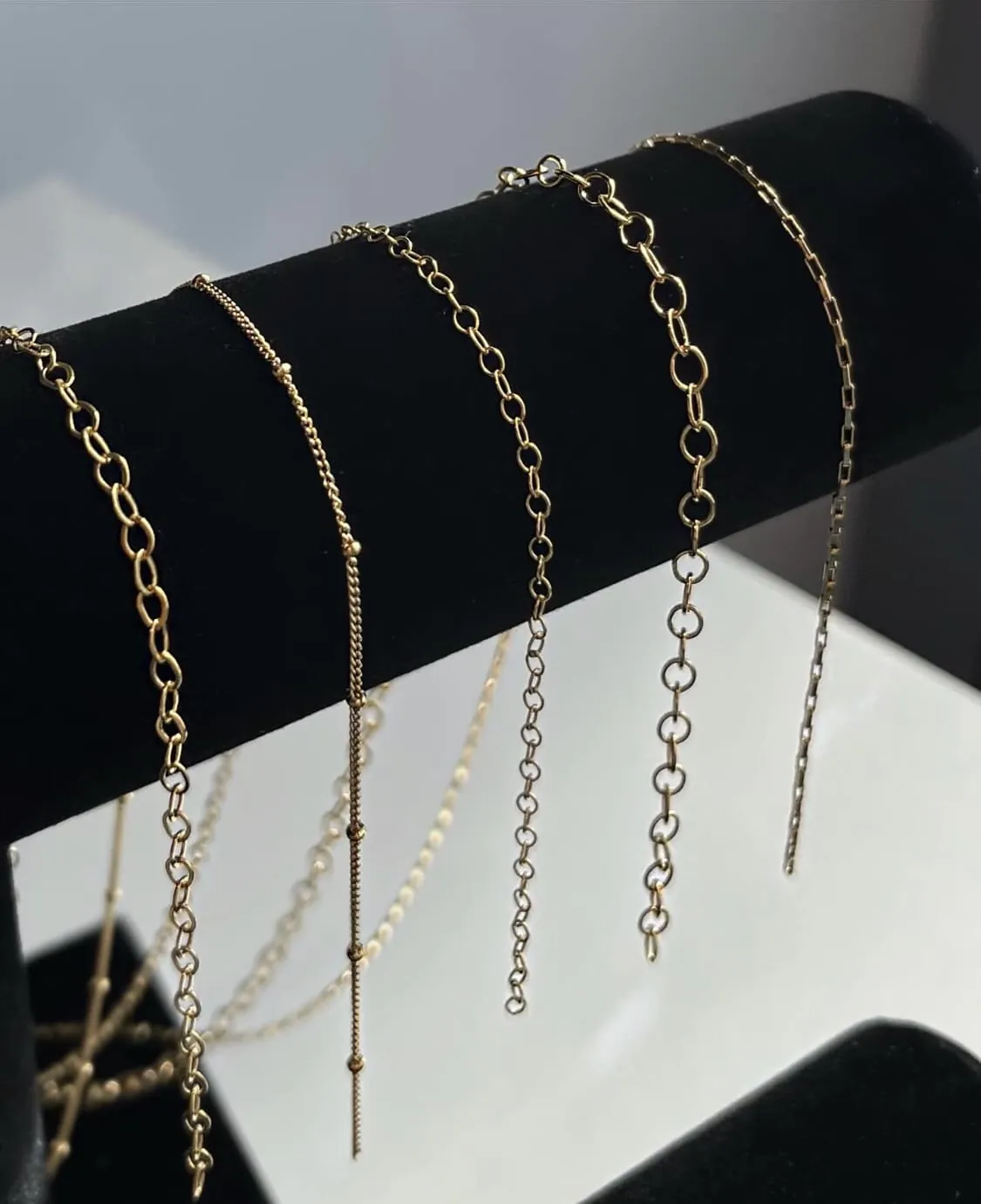 Gold permanent-jewelry chains hanging from a black velvet bar