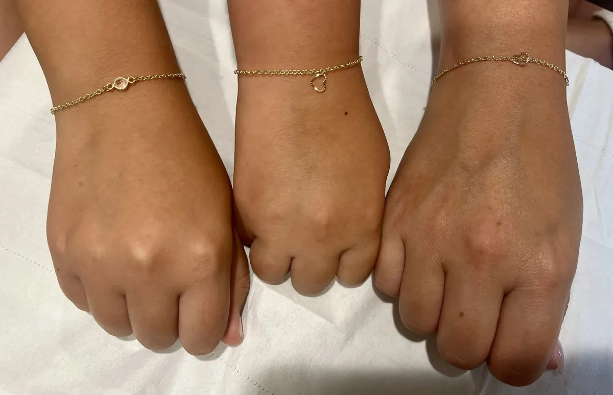 Three wrists wearing fine gold permanent bracelets