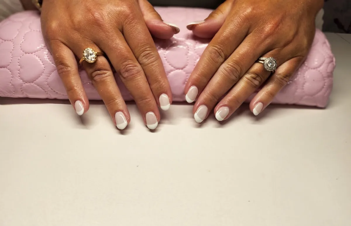 Hands with rings and a white-tipped manicure on a pink nail cushion