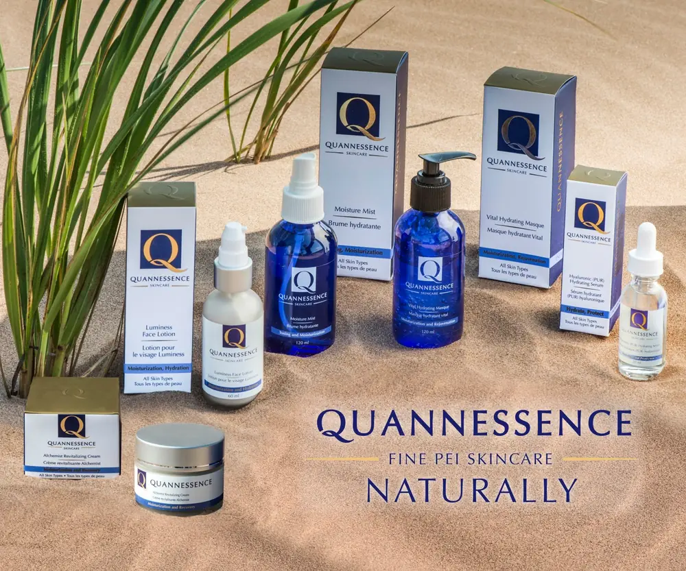 Quannessence skin-care bottles and boxes on sand with grasses